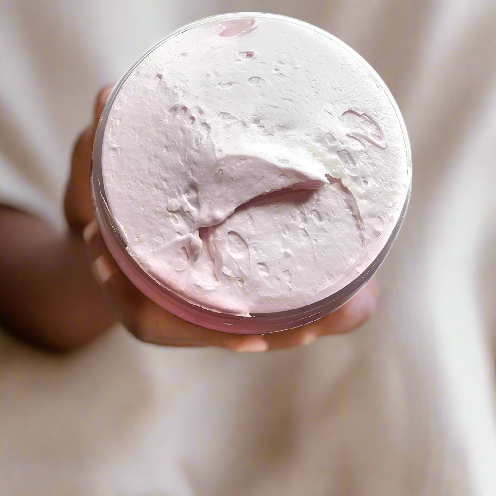Hand holding a pink container of cream against a white background